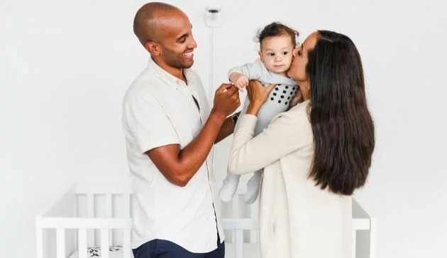 family of three in baby nursery with nanit pro baby monitor in background