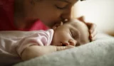 A mother kisses her newborn baby girl's head while she sleeps