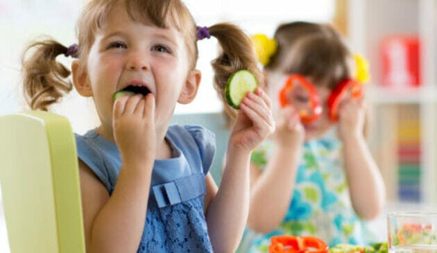 two children eating cucumber and pepper
