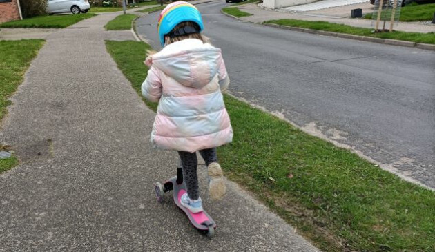 A child using a pink Globber Primo scooter on a residential street