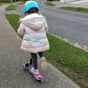 A child using a pink Globber Primo scooter on a residential street