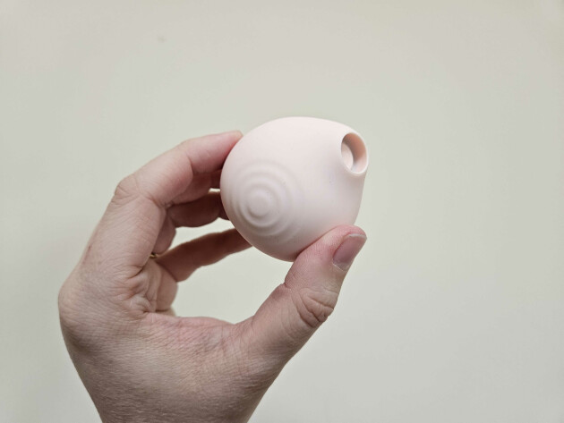 A hand holding the HANX Cindy clitoral suction toy against a wall