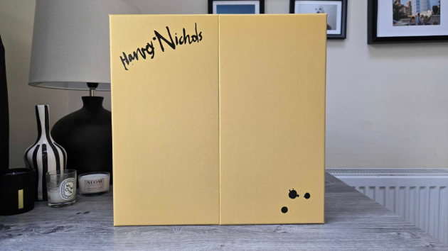 The closed yellow calendar box with two front doors, the Harvey Nichols name in black handwritten-style script at the top left and three black ink splatters at the bottom right