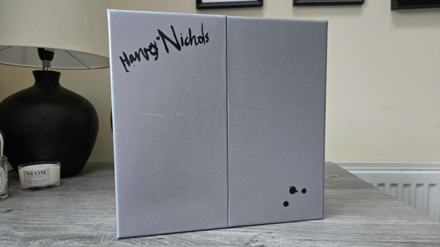 The closed silver-grey calendar box with two front doors, the Harvey Nichols name in black handwritten-style script at the top left and three black ink splatters at the bottom right