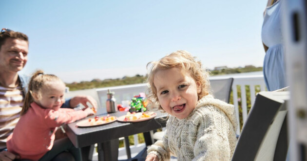 A family eating outside in the sunshine at a Haven holiday park.