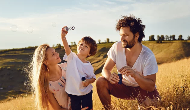 Parents are with their son in a field as he tries to blow bubbles