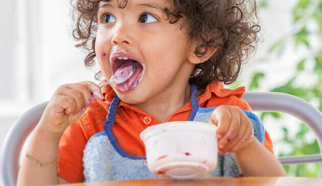 toddler eating yoghurt in highchair