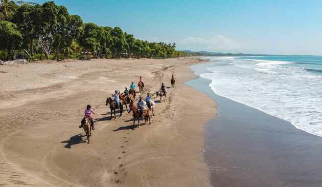 People horse riding across a tropical beach in Costa Rica