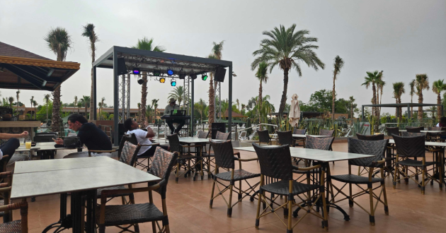 Outdoor poolside terrace with dining tables, woven chairs and a small entertainment stage beneath palm trees