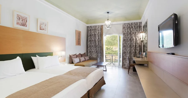 Standard hotel room with twin beds, a sofa bed, wall-mounted television, desk and doors leading to a balcony