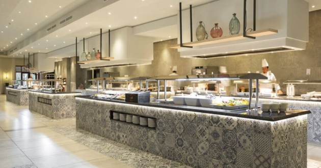 Large hotel buffet with patterned counters, covered food displays and chefs working behind the serving stations