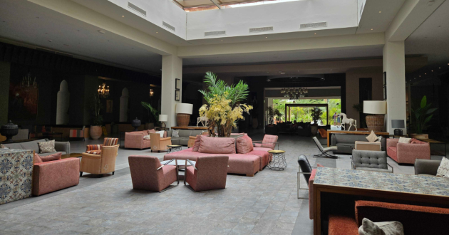 Spacious hotel lobby with pink seating, patterned furniture, indoor plants and a central floral display