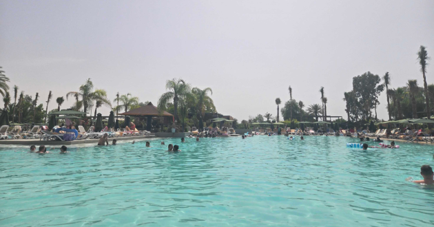 Wide view across the busy main swimming pool, with families in the water and sunloungers lining both sides