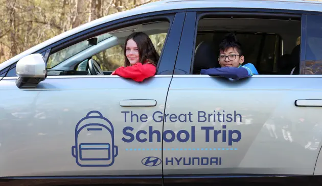 Two children look out of a car window, the car has The Great British School Trip by Hyundai logo on the side