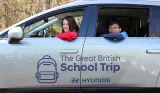 Two children look out of a car window, the car has The Great British School Trip by Hyundai logo on the side