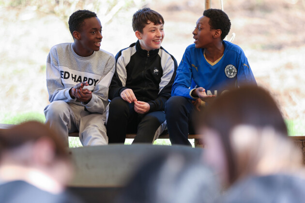 Three teenage boys are sat talking and laughing with each other on a school trip day out