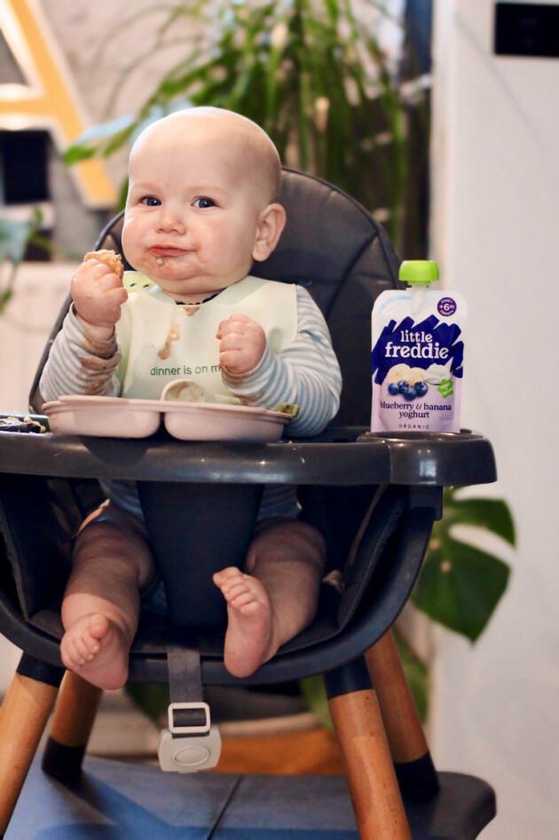 A baby in their highchair eating a Little Freddie food pouch