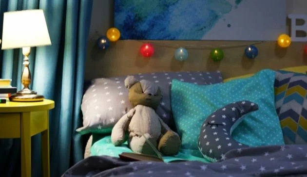 A child's bedroom, there's a teddy bear on the bed and bedsides lamp is on