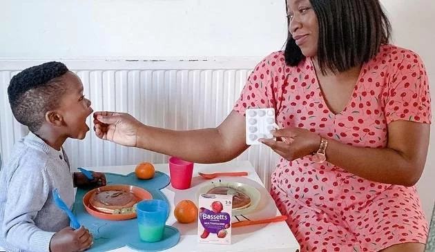 child being fed a multivitamin by mother