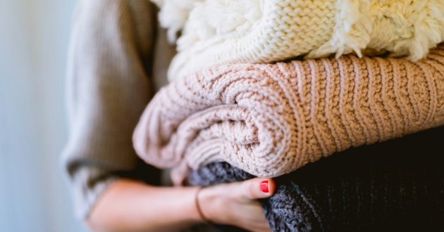 A woman holding a stack of knitwear
