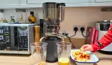 The Kuvings Auto6 slow juicer atop a kitchen worktop with a child putting apple pieces inside of it to make apple juice