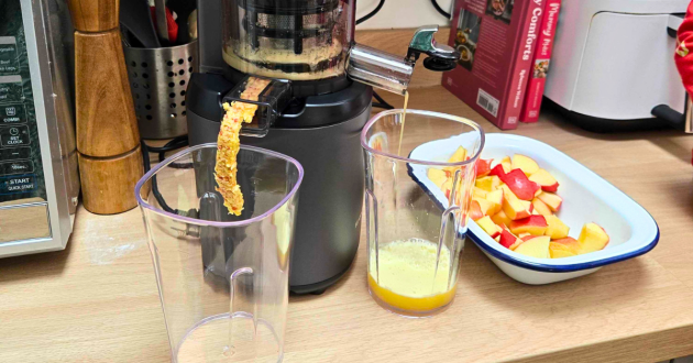 A close up of the Kuvings Auto6 making apple juice, with the pulp being expelled into a jug and the juice into another