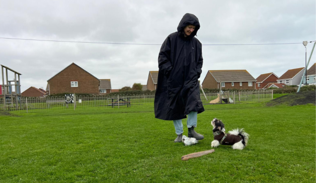 A woman wearing the Lakeland Outdoor Wearable Heated Robe, playing with a small black and white dog