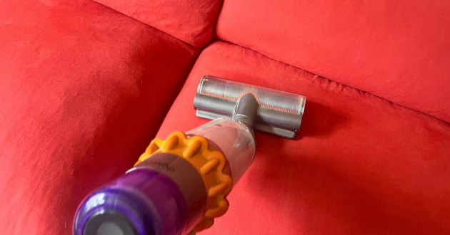 Cordless handheld vacuum cleaning the red twill seat cushion of the Loaf Squishmeister Sofa Bed