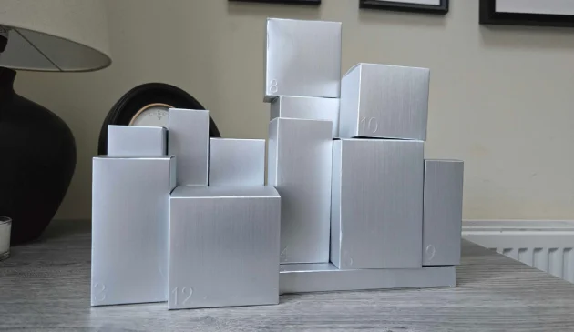 A stack of brushed-silver gift boxes in different sizes, arranged like a city skyline on a grey wooden table, with numbers 3, 4, 5, 8, 9, 10 and 12 embossed on the fronts