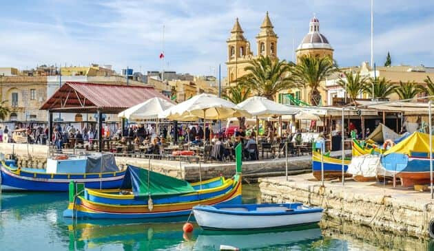 Small colourful boats floating in front of a busy market.