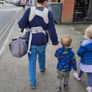 Mum wearing the Mamas & Papas Kudo Baby Carrier and walking alongside 2 children