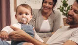 Happy parents holding their young baby with a MAM dummy in his mouth