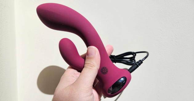 A hand holds the Lovehoney Mantric rabbit vibrator and its charger against a wall in the light