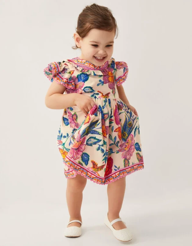 A little girl wears Monsoon's Baby Milena Floral Print Dress Ivory