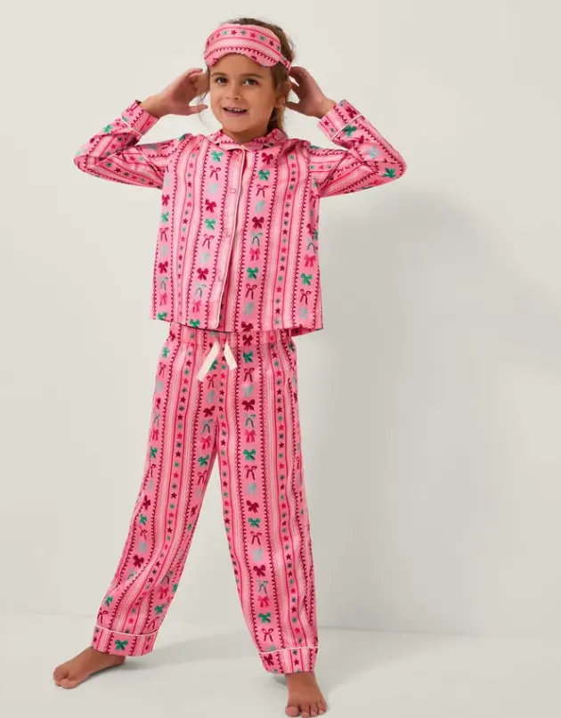 A girl models Monsoon's Bow Print Satin Long Pyjamas & Sleep Mask Set Pink pyjamas