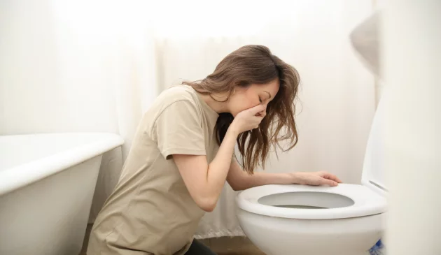 A woman vomits over the toilet
