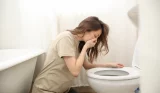 A woman vomits over the toilet