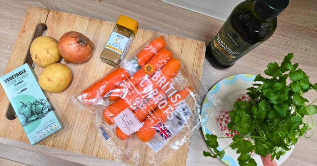 Fresh soup ingredients on wooden board including British carrots, potatoes, onion, stock cubes, herbs and olive oil for recipe