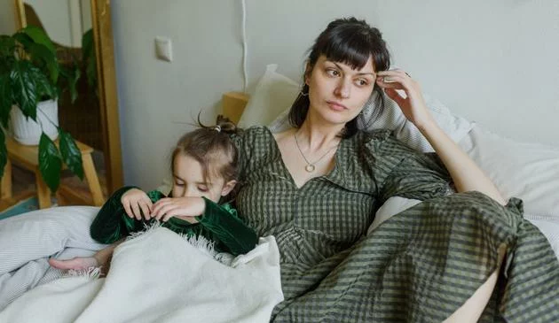 A mother and a daughter resting on a bed.