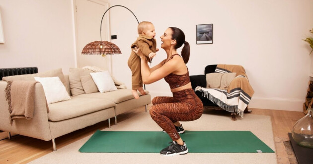A new mother exercises on a yoga mat with her toddler in arms
