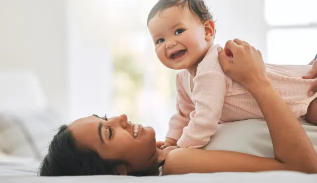 Mother cuddling smiling baby while laying down