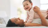 Mother cuddling smiling baby while laying down