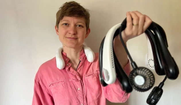 A woman with short hair and a pink shirt wearing a neck fan and holding several more neck fans in her hand