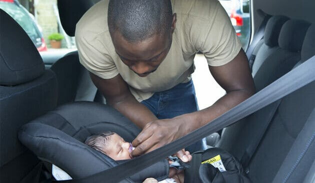 man playing dummy in mouth of newborn baby in car seat