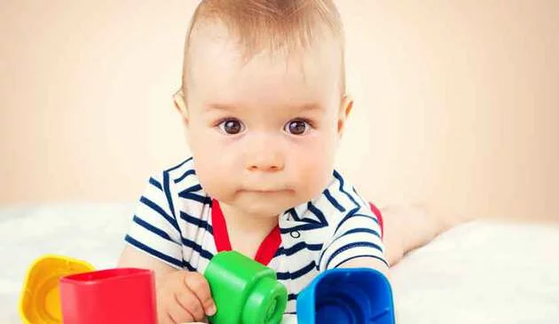 Nine month old baby sitting up playing with toy blocks