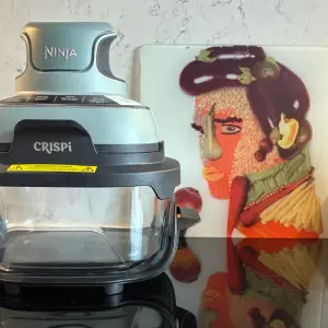 Ninja CRiSPi portable cooking system on kitchen counter next to decorative art and Marmite jar