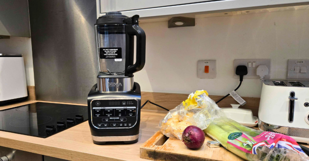 The Ninja Foodi Blender and Soup Maker atop a kitchen worktop next to soup ingredients