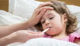Child in bed having temperature taken with thermometer