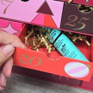 Drawer 20 of the OK! Beauty Advent Calendar open to reveal a turquoise Dr.PAWPAW lip balm surrounded by shredded gold paper