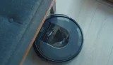 Black iRobot robot vacuum poking out from underneath a grey sofa